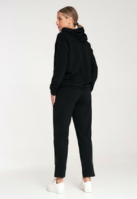 Czarny zestaw bluzy i spodni wykonany z miękkiego materiału. Bluza ma sznurek do regulacji i kieszeń kangurzką; spodnie mają zwężany krój i elastyczny pas.