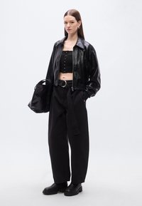 Μαύρο κοντό δερμάτινο μπουφάν, μαύρο εφαρμοστό τοπ με λεπτομέρεια κουμπιών, φαρδιά μαύρη παντελόνα με ζώνη και μαύρα μποτάκια αστραγάλου. Συμπεριλαμβάνεται μαύρη τσάντα.