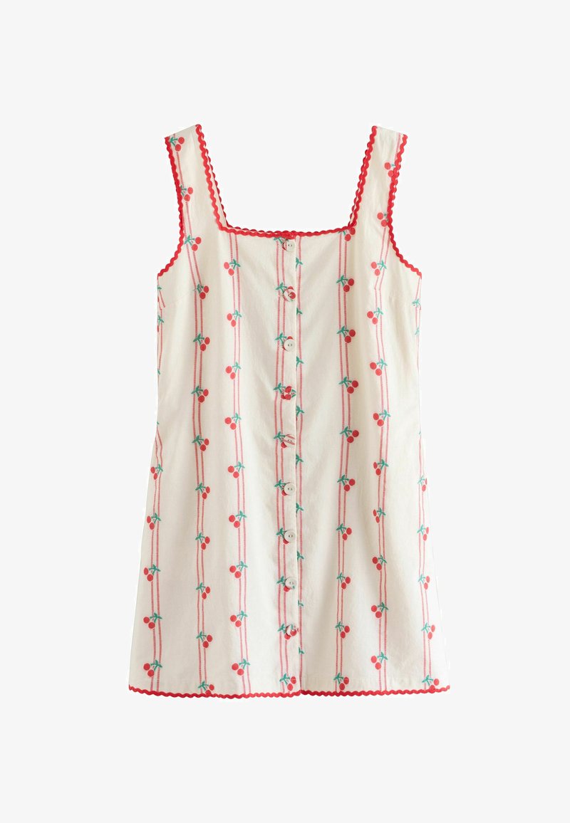 Robe sans manches en coton blanc, avec des bordures festonnées rouges, une fermeture à boutons sur le devant, et un motif répétitif de cerises avec des feuilles vertes le long de lignes verticales.