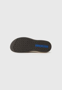 Sorte gummisåle med et strukturert mønster som har bølgende linjer; "BIRKENSTOCK" er trykket i blått langs midten.