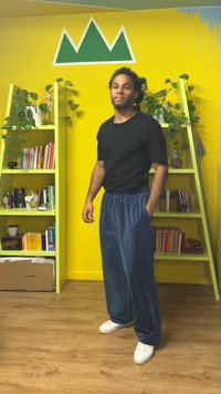 Zwart kort mouwshirt, blauwe loszittende joggingbroek met zakken, witte sneakers, binnenomgeving met gele muren en groene accenten.