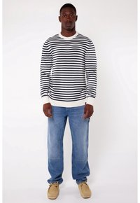 Pull rayé à manches longues bleu marine et blanc avec un col rond, associé à un jean bleu clair ample et des chaussures beiges.