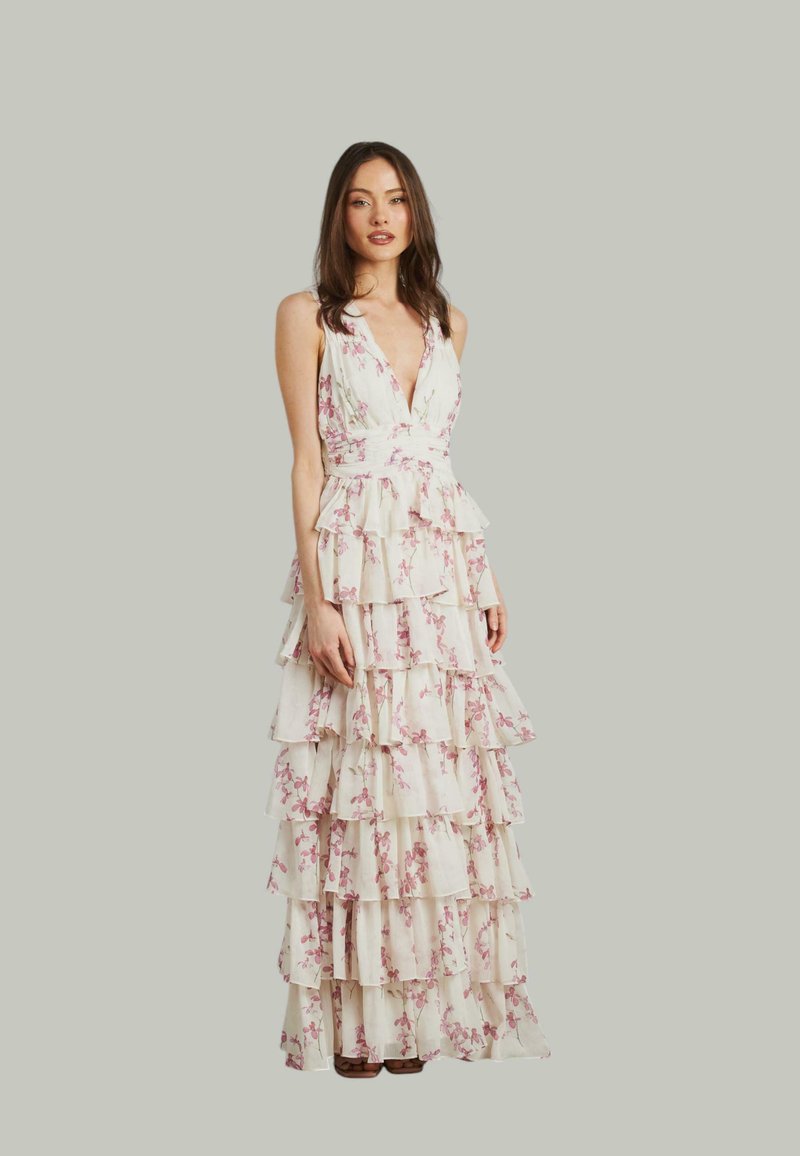 Maxi-jurk van lichte stof met een bloemenpatroon, voorzien van een diepe V-hals, gelaagde ruches en een getailleerde taille. De kleuren zijn voornamelijk wit met roze accenten.