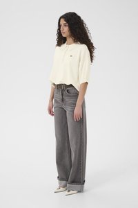 Krēmkrāsas polo krekls ar apkakli un trim pogām, kombinēts ar plašām pelēkām džinsu biksēm. Apavi ir ar gaišām, smailām papēžiem.