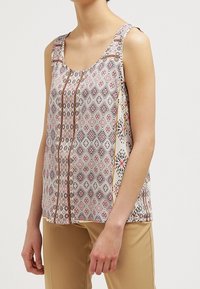 Top sans manches avec un motif géométrique dans des tons de crème, rose et noir, de forme scoop et avec des accents décoratifs sur les côtés.