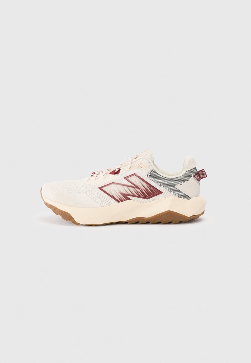 Baskets athlétiques blanches et beiges avec un logo "N" bordeaux, une semelle texturée et un passant au talon, montrées de profil sur un fond uni.