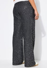 Pantalones de pierna ancha en negro, cubiertos de lentejuelas plateadas, con una superficie texturizada. La cintura se asienta cómodamente, con un ajuste relajado y piernas rectas.