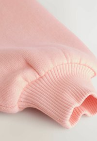 Felpa rosa chiaro con maniche a costINE e texture, superficie liscia e vestibilità leggermente rilassata.