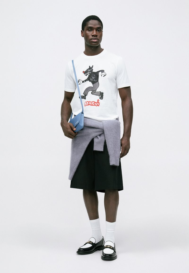 Witte t-shirt met een zwart grafisch ontwerp en rode "Marni" tekst, gecombineerd met zwarte shorts, een lila trui eroverheen gedrapeerd, en zwarte instappers.