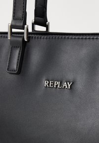 Svart lærveske med sølvfarget detaljer, med "REPLAY"-logoen. Overflaten har en glatt tekstur og ryddig søm langs kantene.