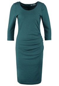 Robe ajustée turquoise avec manches trois-quarts, encolure ronde et fronces latérales. Confectionnée dans un tissu doux et extensible. Longueur mi-mollet.