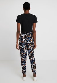 Top corto nero abbinato a pantaloni jogger con stampa floreale in blu navy, caratterizzati da fiori bianchi e arancioni, vita elasticizzata e polsini alla caviglia.