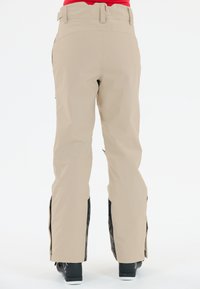 Beige Schneehosen mit geradem Schnitt, mit schwarzen Seitenpaneelen, glatter Textur und Reißverschlussbelüftungen an den Knöcheln.