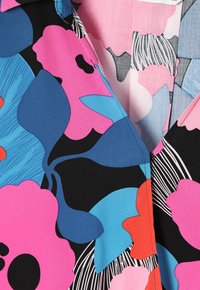 Primo piano di un tessuto con un audace motivo floreale in rosa, blu, nero, rosso e bianco, che mostra dettagli nitidi e cuciture sui fiori colorati.