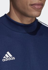 Granatowy sweter z wysokim kołnierzem, z białym logo Adidas na lewej piersi oraz trzema białymi paskami na ramionach, wykonany z gładkiego materiału.