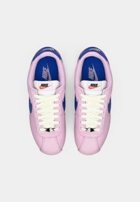 Ζεύγος ροζ και μπλε αθλητικών παπουτσιών Nike με λευκές κορδόνες, φαίνεται από πάνω σε λευκό φόντο.