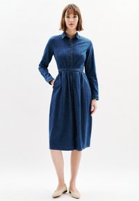 Sukienka koszulowa dżinsowa w ciemnoniebieskim kolorze, z kołnierzykiem, zapinana na guziki z przodu, z długimi rękawami i paskiem w talii. Gładka tekstura, do długości midi.