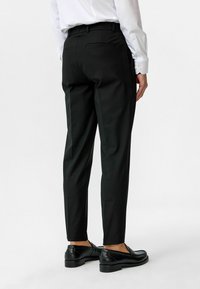 Zwarte op maat gemaakte broeken met een slim fit, met een gladde textuur, riemlussen en twee achterzakken, gecombineerd met zwarte instappers.