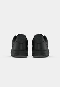 Par de sapatilhas Nike Air pretas mostradas por trás em um fundo branco, apresentando couro texturizado e detalhes do logótipo.