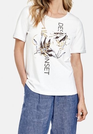 Weißes Baumwoll-T-Shirt mit kurzen Ärmeln, das ein schwarzes und goldenes Grafikdesign mit botanischen Elementen und dem Text "DESERT SUNSET" zeigt.
