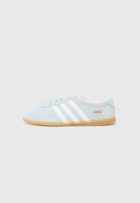 Gaiši zili Adidas Gazelle apavi ar baltām svītrām un gumijas zoli, izvietoti uz vienkārša balta fona.