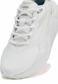 Baltas sneakers ar teksturētu sietu augšdaļu, mīkstu valni un šņorēm. Iespējas ar smalku zīmolu un gumijas zoli ar raupjumu.
