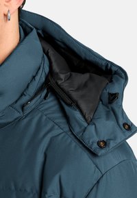 Grove pufferjack met een hoge kraag, zwarte voering, ritsdetails en drukknoopsluiting. Glad, waterafstotend stof met een gewatteerde textuur.