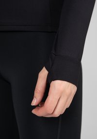 Schwarzes, athletisches Langarmoberteil mit einem taillierten Design. Es verfügt über Daumenlöcher an den Bündchen, glattes, elastisches Material und flache Nähte.