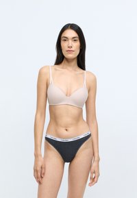 Jasnoróżowy biustonosz z cienkimi ramiączkami i formowanymi miseczkami, w zestawie z ciemnoszarymi majtkami bikini z białym paskiem Calvin Klein.