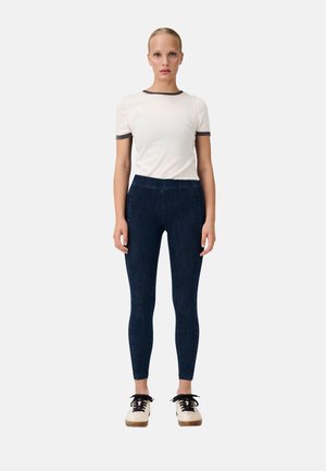 Witte top met korte mouwen en donkergrijze details, gecombineerd met donkerblauwe skinny jeans en beige plateau schoenen met zwarte veters.