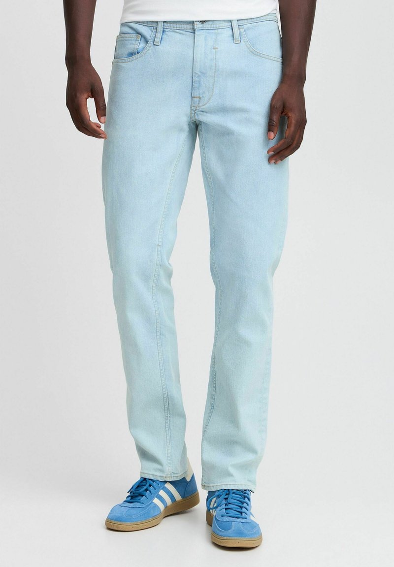Jeans de mezclilla azul claro con corte recto, diseño de cinco bolsillos y detalles de costura en contraste. Combinados con zapatillas deportivas azules.