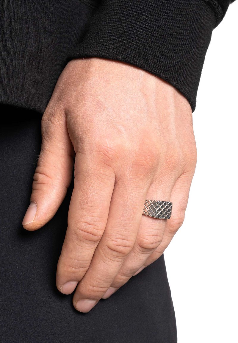 Ασημένιο μέταλλο δαχτυλίδι με υφή που μοιάζει με διαμάντια. Φορεμένο σε χέρι, με ορατό χρώμα δέρματος και μαύρο ένδυμα στο φόντο.