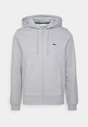 Sweat à capuche zippé gris clair avec poches avant, capuche à cordon, et petit logo crocodile vert sur la poitrine gauche.
