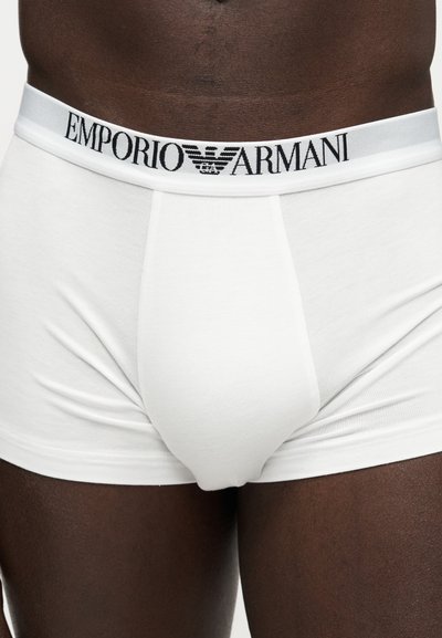 Άσπρα μποξεράκια Emporio Armani που φοριούνται από άτομο με σκούρο δέρμα, με ελαστική ζώνη με μαύρο κείμενο και λογότυπο.