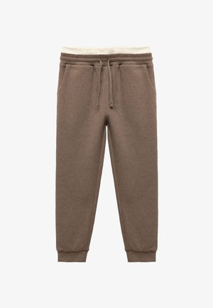 Pantalons de survêtement bruns à texture avec taille élastique et cordon de serrage, présentant des accents crème. Les poignets sont ajustés aux chevilles.