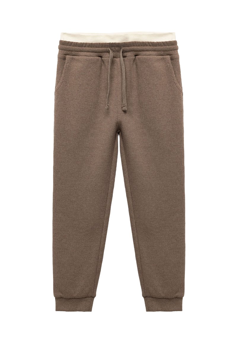 Braune, strukturierte Jogginghosen mit elastischem Bund und Kordelzug, versehen mit Cremetönen. Die Bündchen sind eng an den Knöcheln.