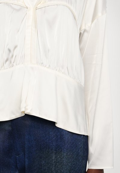 Vit satinkjol med långa ärmar, veckat mönster och utsvängd nederkant. Inkluderar en knäppt framplacket och slät textur, matchad med mörk denim.