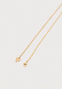 Κολιέ με αλυσίδα σε χρυσαφί τόνο με τριγωνικό μενταγιόν και κούμπωμα. Διαθέτει χαραγμένο λογότυπο στο μενταγιόν, λείες συνδέσεις και λεπτή υφή.