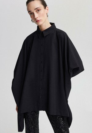 Black oversized button-up shirt with a classic collar, wide sleeves, and a smooth texture, paired with sequined black leggings.
