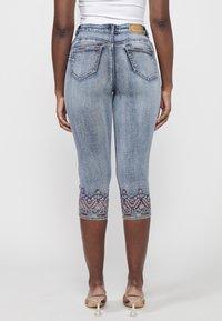 Helle blaue Jeans-Caprihosen mit taillierter Passform. Ausgestattet mit aufwendiger, bunter Bestickung am Saum und klassischen Gesäßtaschen.