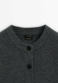 Harmaa villatakki, jossa on pyöreä kaula-aukko, röyhelöhihet, kolme mustaa nappia edessä ja kangasmerkki sisäpuolella.