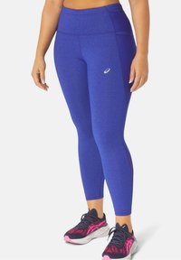 Leggings sportivi blu realizzati in tessuto elasticizzato, con vita alta e pannelli laterali. Indossati con scarpe da corsa nere e rosa.