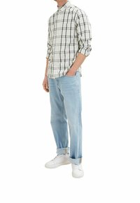 Camisa de cuadros en crema, azul marino y verde; pantalones vaqueros de corte relajado en azul claro; zapatillas blancas; puños de los pantalones doblados.