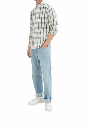 Camicia a quadri nei colori crema, blu navy e verde; jeans blu chiaro a vestibilità comoda; sneaker bianche; risvolti sui jeans.