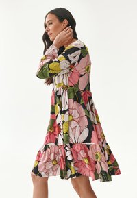 Blumenkleid mit langen Ärmeln, das große rosa, weiße und gelbe Blumen auf schwarzem Hintergrund zeigt. Rüschensaum und lockere Passform.