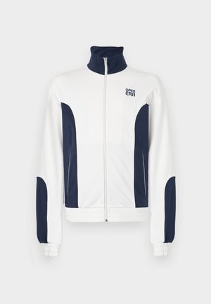 White zip-up jacket with navy blue accents on the sides and sleeves. Stand-up collar, elastic cuffs, and logo on the chest. Smooth fabric.