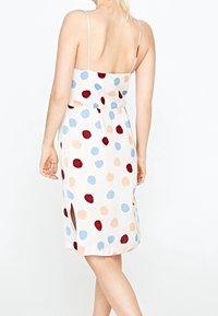 Vestido sin mangas y sin espalda con una cintura ajustada. Presenta una tela color crema con grandes lunares rojos, azules y melocotón, y rendijas laterales.