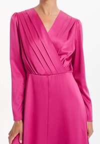 Robe portefeuille en satin fuchsia à manches longues, avec des détails plissés sur le corsage et une silhouette lisse jusqu'au sol.