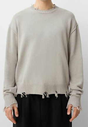 Light gray long-sleeve sweater with intentional frayed edges on collar, cuffs, and hem worn with black pants.