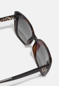 Acetate sunglasses with oversized square frames, dark gray lenses, and tortoiseshell pattern on temples. Features silver hardware detail.